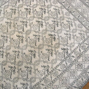 Geometric tribal pattern in gray on a cream ground, showing multiple patterned borders on wood floor.
