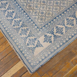 Low pile rug in faded blue and ivory geometric patterns covers worn diagonal wood planks.