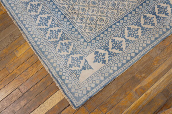 Low pile rug in faded blue and ivory geometric patterns covers worn diagonal wood planks.