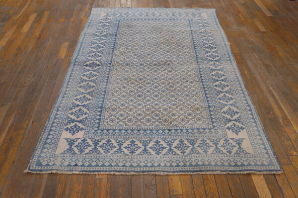 Rectangular low-pile rug in blue and cream geometric designs placed on worn wood planks.