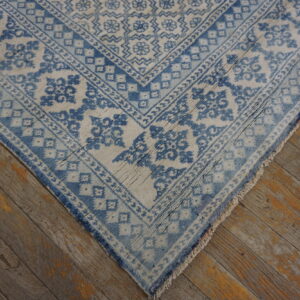 Faded blue and off-white rug with bordered patterns, showing tassels on distressed wood floor.