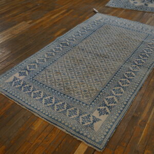 Blue and light beige low-pile patterned rug displayed on rustic, dark brown hardwood plank flooring.