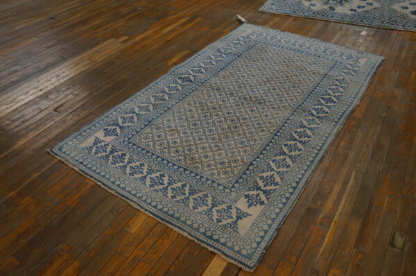 Blue and light beige low-pile patterned rug displayed on rustic, dark brown hardwood plank flooring.