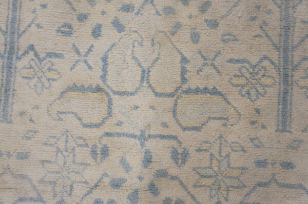 Detail of a shaggy rug featuring blue outline patterns over a thick, creamy beige pile.