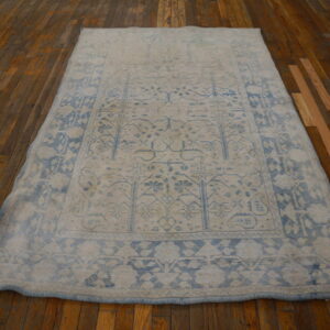 Muted blue and cream patterned area rug resting on shiny dark brown plank flooring.