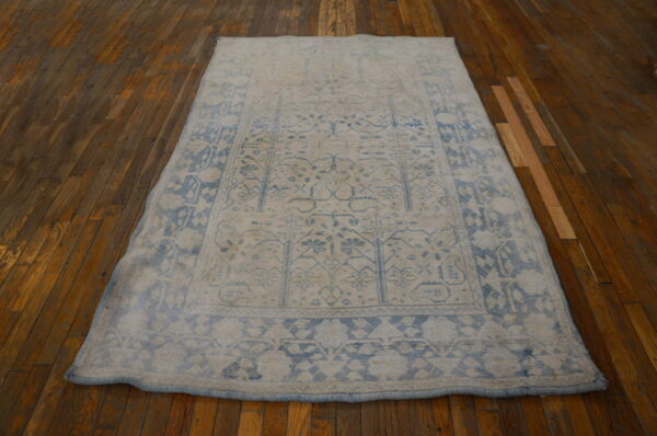 Muted blue and cream patterned area rug resting on shiny dark brown plank flooring.