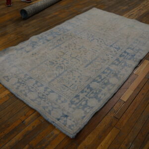 Faded traditional rug in muted blue and light gray rests on dark brown wood plank flooring.