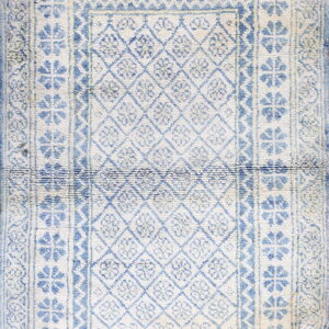 Textured cream and blue rug with a central geometric diamond pattern and wide repeating floral borders.