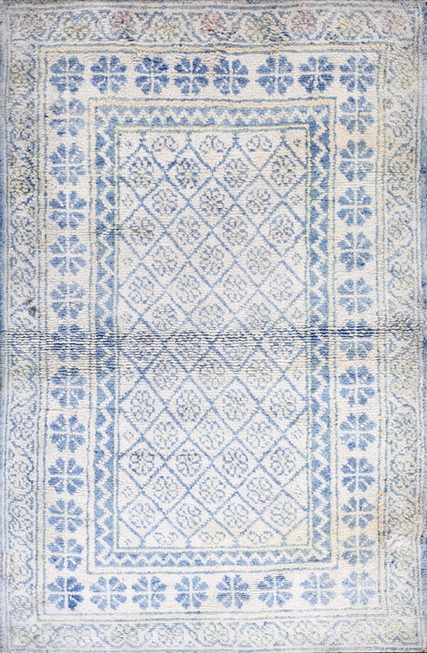 Textured cream and blue rug with a central geometric diamond pattern and wide repeating floral borders.