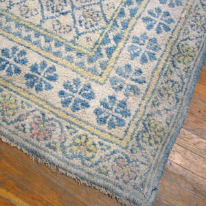 Corner of a textured blue and cream floral rug laid over worn, warm brown hardwood planks.