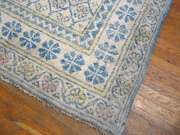 Corner of a textured blue and cream floral rug laid over worn, warm brown hardwood planks.
