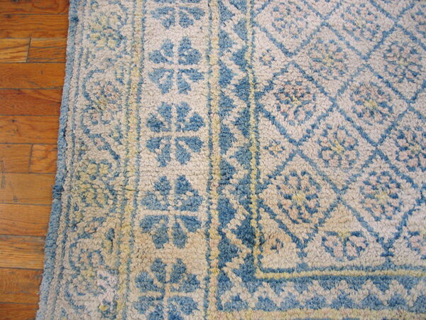 High-pile blue and cream geometric rug with stylized floral patterns borders natural wood flooring.