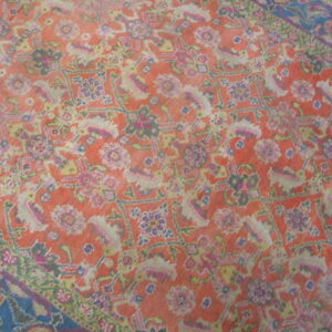 Distressed traditional rug featuring an orange-red field, ornate floral patterns, and a dark blue patterned border.