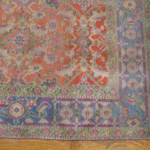 Low-pile rug section in coral, blue, green, and pink traditional floral patterns on light brown wood flooring.