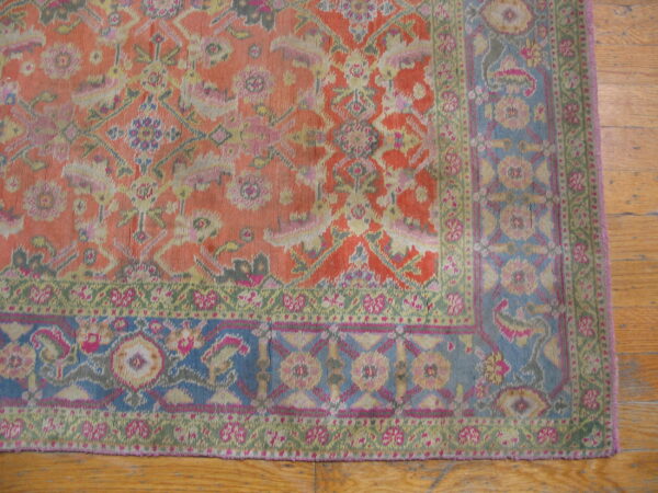 Low-pile rug section in coral, blue, green, and pink traditional floral patterns on light brown wood flooring.