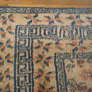 Beige rug with distressed blue geometric borders and scattered coral and teal floral patterns rests on wood.