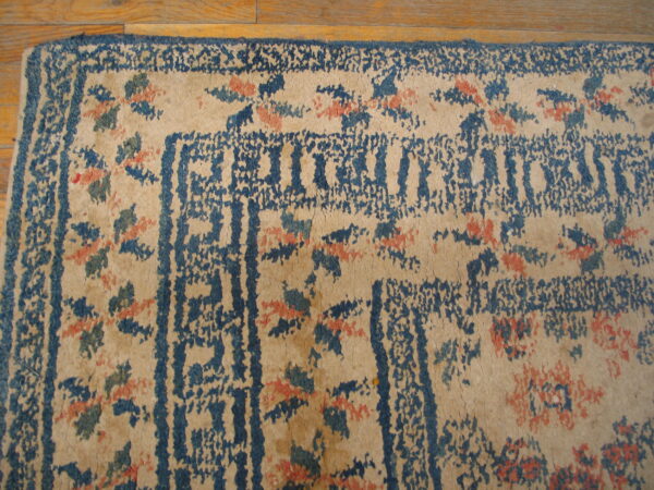 Beige rug with distressed blue geometric borders and scattered coral and teal floral patterns rests on wood.