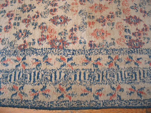 Worn low-pile rug in beige, deep blue, and coral featuring abstract floral motifs and a distressed border.