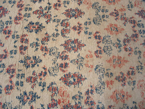 Close-up of a severely cracked beige surface with scattered distressed blue and red abstract floral motifs.