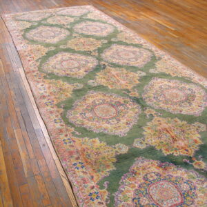Long green runner rug with large yellow and pink floral medallions placed on plank wood flooring.