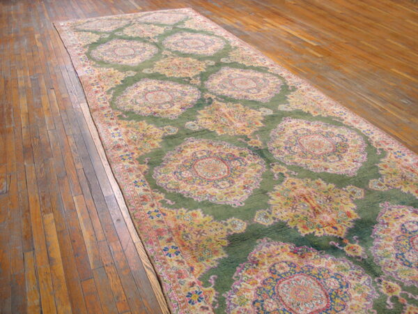 Long green runner rug with large yellow and pink floral medallions placed on plank wood flooring.
