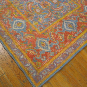 Textured coral, blue, and yellow traditional rug corner rests on distressed honey-toned hardwood flooring.