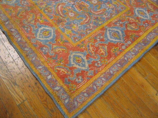Textured coral, blue, and yellow traditional rug corner rests on distressed honey-toned hardwood flooring.