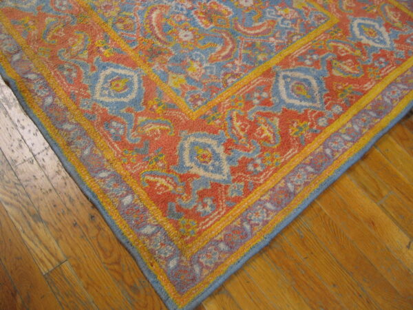 Faded traditional rug features coral, blue, and gold colors against worn medium-toned plank flooring.