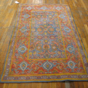 A brightly colored rug with blue, coral, and yellow traditional patterns rests on wooden floorboards.