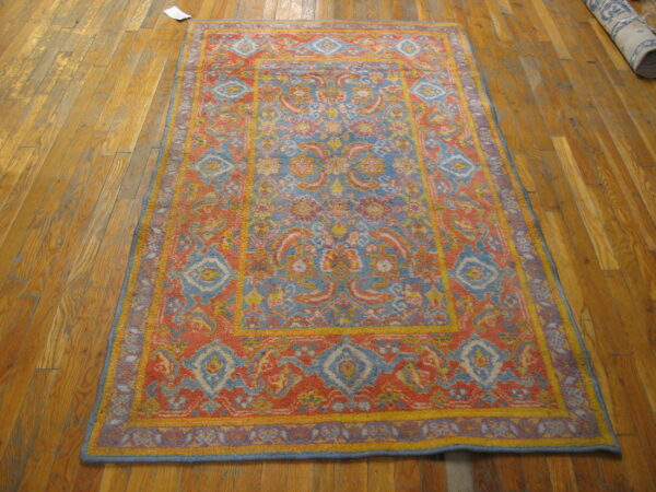 A brightly colored rug with blue, coral, and yellow traditional patterns rests on wooden floorboards.
