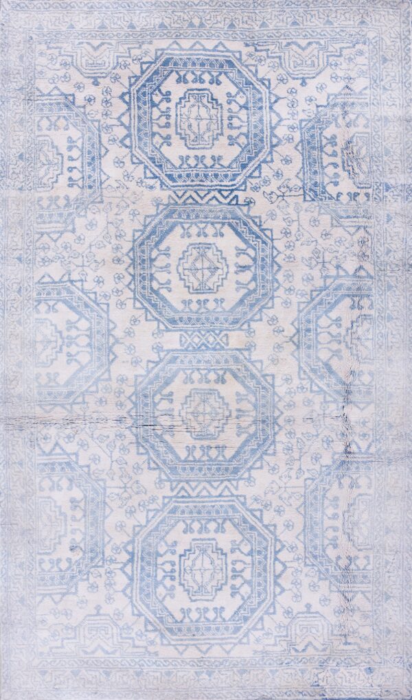 A rectangular low-pile rug with faded blue geometric octagonal patterns is laid on polished wood flooring.