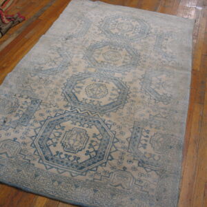 Faded light blue geometric rug on a beige field, resting on glossy plank hardwood floors.