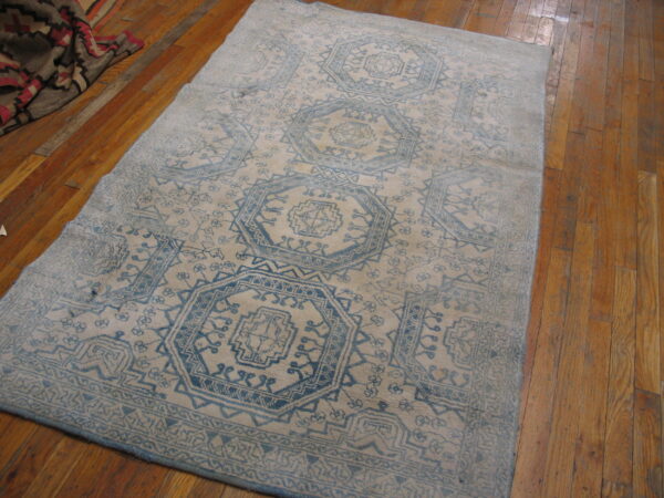 Faded light blue geometric rug on a beige field, resting on glossy plank hardwood floors.