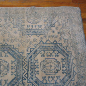 Low pile rug with blue geometric tribal patterns on a cream field rests on hardwood floors.