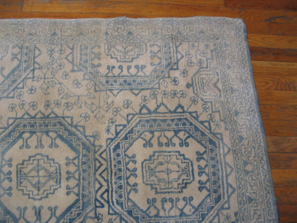 Low pile rug with blue geometric tribal patterns on a cream field rests on hardwood floors.