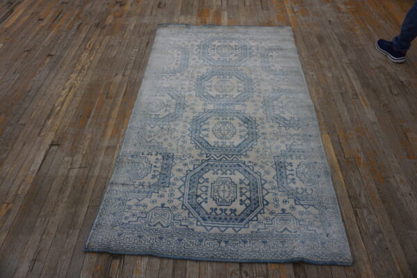 Blue and white geometric pattern rug with visible distressing rests on worn, wide wooden floorboards.