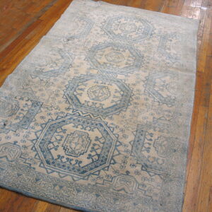 Distressed blue and beige geometric rug featuring repeating medallions lies on a glossy plank wood floor.