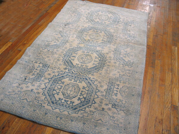 Distressed blue and beige geometric rug featuring repeating medallions lies on a glossy plank wood floor.
