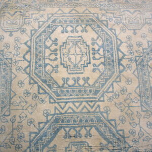 Distressed, high-pile beige rug featuring a repeating light blue geometric medallion design.