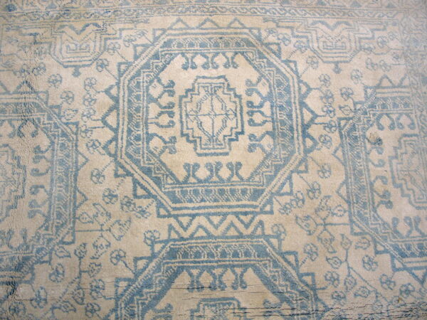Distressed, high-pile beige rug featuring a repeating light blue geometric medallion design.