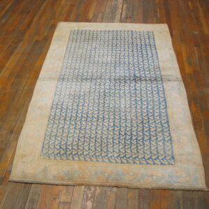 Faded blue and tan rug featuring a repeating pattern and broad border on rustic wood floors.