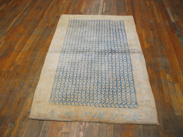 Faded blue and tan rug featuring a repeating pattern and broad border on rustic wood floors.