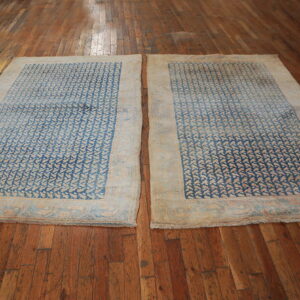 Two rugs with blue and beige repeating geometric designs are displayed side-by-side on brown wood floors.