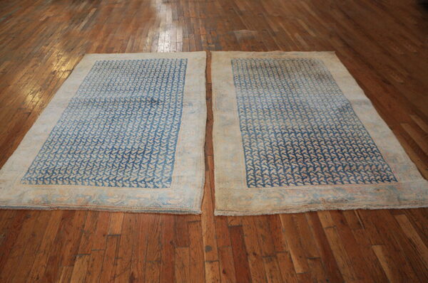 Two rugs with blue and beige repeating geometric designs are displayed side-by-side on brown wood floors.