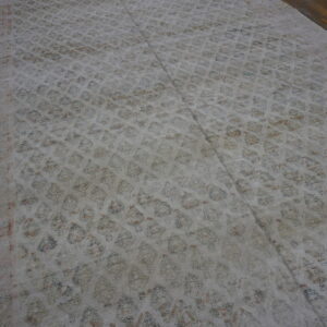 Muted, low-pile rug with repeating blue and rust motifs covers dark wooden floorboards.