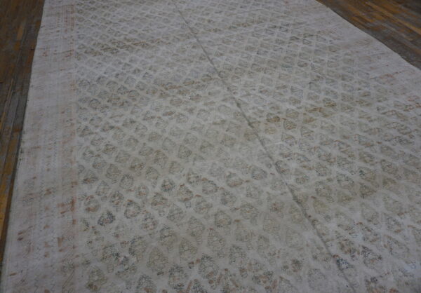 Muted, low-pile rug with repeating blue and rust motifs covers dark wooden floorboards.