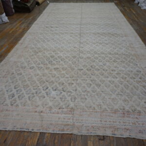 Large distressed pale beige rug with muted blue pattern displayed on brown hardwood planks in a storage area.