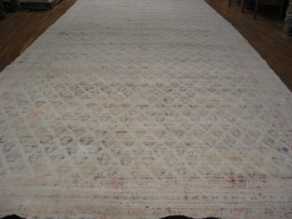 An oversized, faded cream rug with subtle blue and pink floral patterns covers dark wood floor.