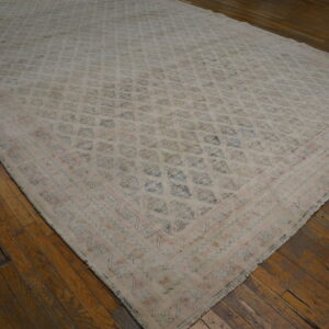 Low-pile, muted beige rug with a faded blue geometric pattern and pink border on a dark wood plank floor.