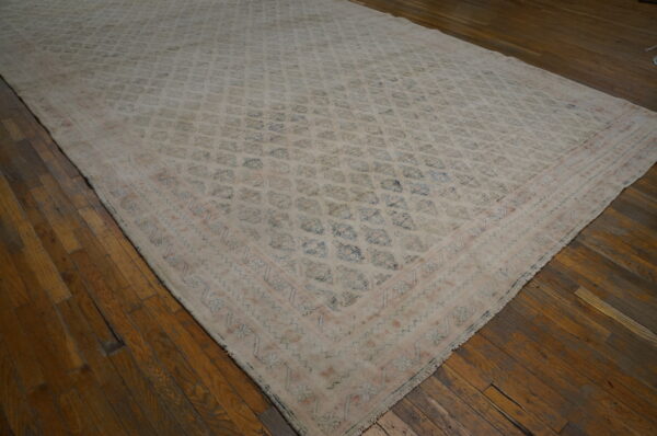 Low-pile, muted beige rug with a faded blue geometric pattern and pink border on a dark wood plank floor.